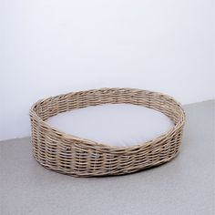 a round wicker basket with white cushion on the floor next to a gray wall