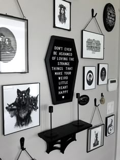 a black and white photo of a wall with many framed pictures on it, including a sign that says don't ever be afraid of loving the strange