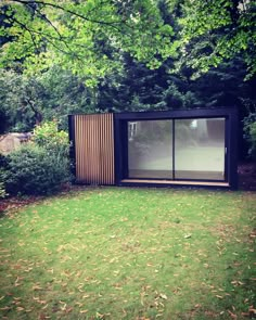 a small wooden structure sitting in the middle of a lush green field next to trees