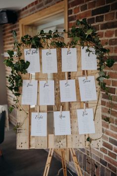 a wooden easel with seating cards attached to it and greenery growing on top