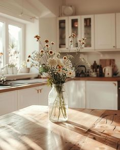 a vase filled with white flowers sitting on top of a wooden table in a kitchen