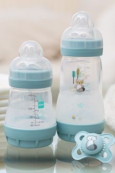 two baby bottles sitting on top of a table next to a pacifier and spoon