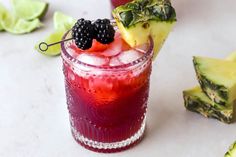 two glasses filled with fruit and garnish next to slices of pineapple