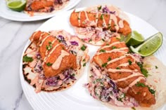 fish tacos with cole slaw and lime wedges on white plates, ready to be eaten