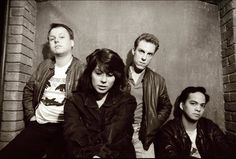 four people are posing for a photo in front of a brick wall and one is wearing a leather jacket