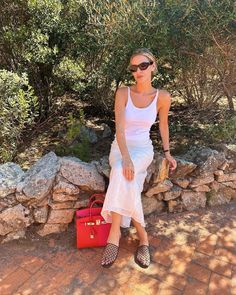 a woman sitting on a stone wall next to a red bag