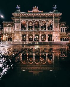 a large building with statues on the top of it's roof and water in front of it