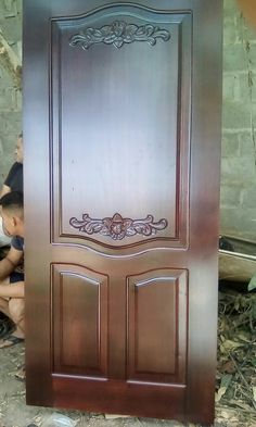 a young boy sitting on the ground next to a wooden door that has been painted brown