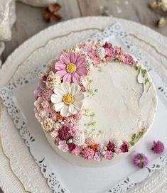 a white cake with flowers on it sitting on a plate next to some doily