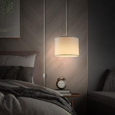 a bed sitting under a lamp next to a night stand with a clock on it