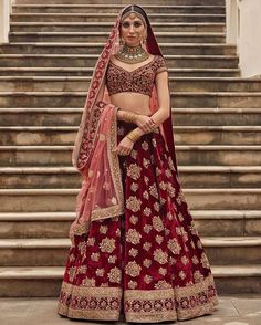 a woman in a red and gold bridal gown standing on steps with her hands behind her head