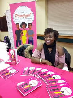 a woman sitting at a table in front of a pink sign that says the powerful