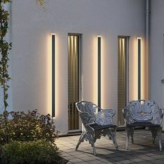 three chairs and two tables sitting in front of a white building with lights on it