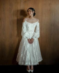 a woman wearing a white dress standing in front of a wooden wall with her hands on her hips