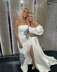 two women in white gowns posing for the camera with one holding her leg up