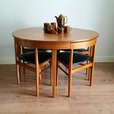 a wooden table with two chairs and a teapot on top of it in front of a white wall