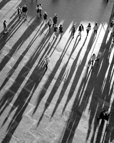 black and white photo of people walking down the street with their shadows on the ground