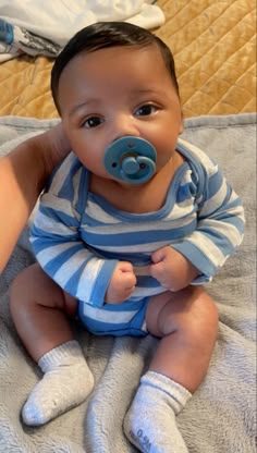 a baby with a pacifier sitting on a bed