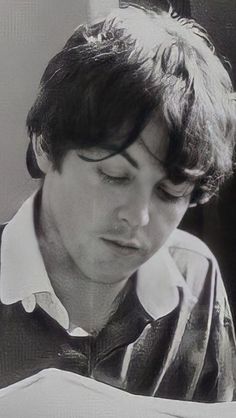 black and white photograph of a young man looking at something in his hand while reading a book