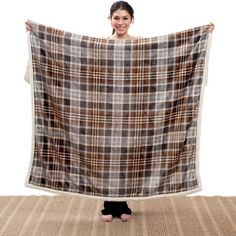 a woman holding up a plaid blanket in front of her face and standing on the floor