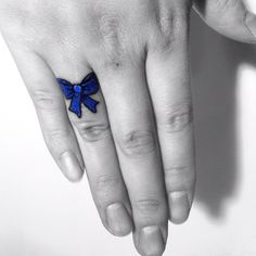 a woman's hand with a blue bow tattoo on her left thumb and finger