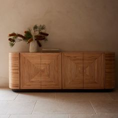 a vase with flowers on top of a wooden cabinet in front of a beige wall