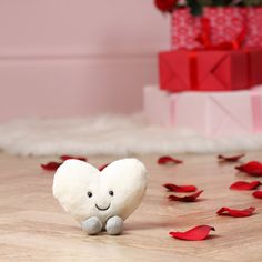 a stuffed heart sitting on top of a wooden floor next to a pile of red rose petals