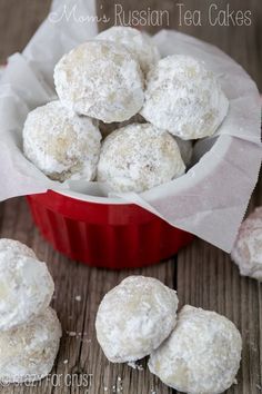 a red bowl filled with snowball cookies on top of a wooden table