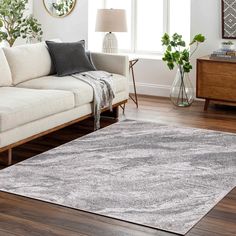 a living room with a couch, chair and rug on the hardwood floor in front of a window