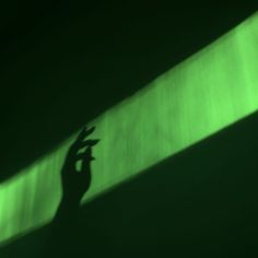 the shadow of a person's hand on a green wall with light coming through it