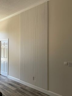 an empty room with hard wood flooring and white vertical blinds on the wall behind it