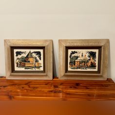 two framed pictures sitting on top of a wooden shelf