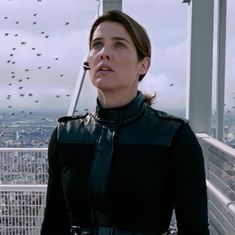 a woman standing on top of a building with birds flying in the sky above her