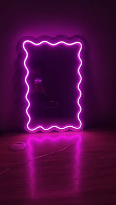 a purple neon frame sitting on top of a wooden floor in front of a wall