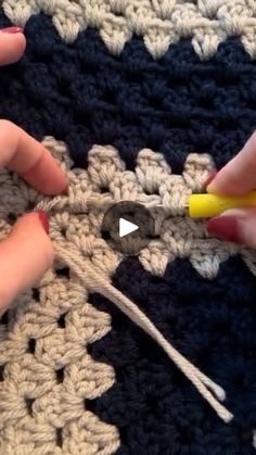 two hands are crocheting together on a piece of yarn with a yellow handled crochet hook