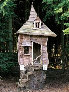 a tree house built into the side of a tree stump in front of some trees