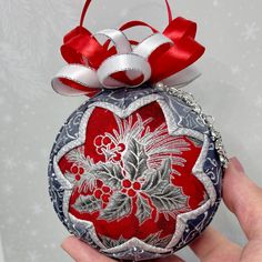 a hand holding an ornament decorated with red and white flowers, bows and snowflakes