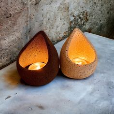 two candles sitting on top of a table next to a stone wall and cement slab