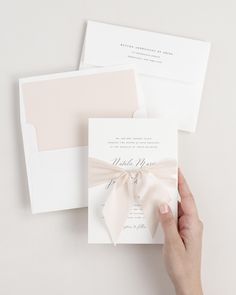 a hand holding an envelope with a bow on the front, and a wedding card in the back