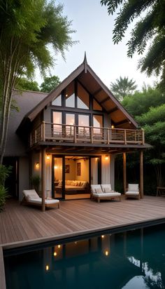 a house that is next to a pool with chairs on the deck and trees in the background