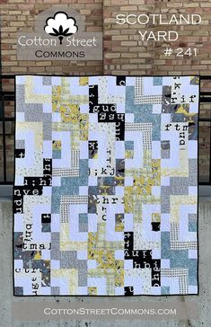 a blue and yellow quilt hanging on the side of a brick wall next to a sign that says cotton street yard