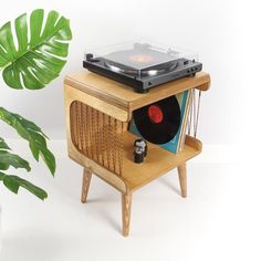 an old record player is sitting on a stand next to a potted green plant