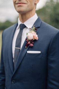 a man wearing a suit and tie with a flower in his lapel pocket, looking at the camera