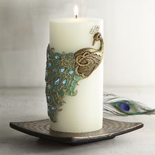 a candle with a peacock design on it sitting on a plate next to a peacock feather