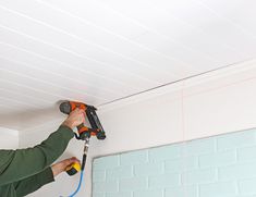 a man using a power drill to install a ceiling in a room with white walls