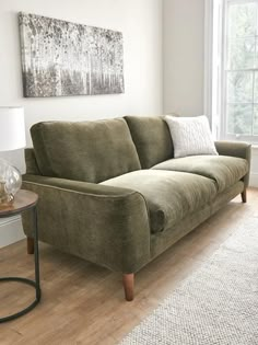 a green couch sitting on top of a hard wood floor next to a table with a lamp