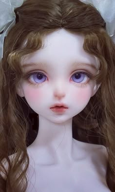 a close up of a doll with long hair wearing a white dress and big blue eyes