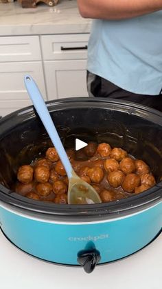 a slow cooker filled with meatballs on top of a counter next to a person holding a spoon