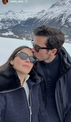 a man and woman standing next to each other on top of a snow covered slope