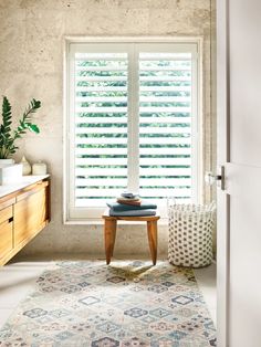 a room with a rug, table and large window that has shutters on it